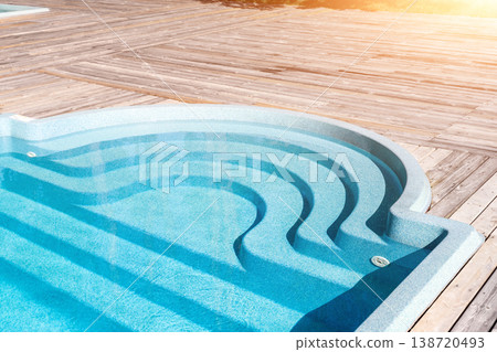 New modern fiberglass plastic swimming pool entrance step with clean fresh refreshing blue water on bright hot summer day at yard or resort hotel spa area. Wooden flooring deck of teak or larch board 138720493