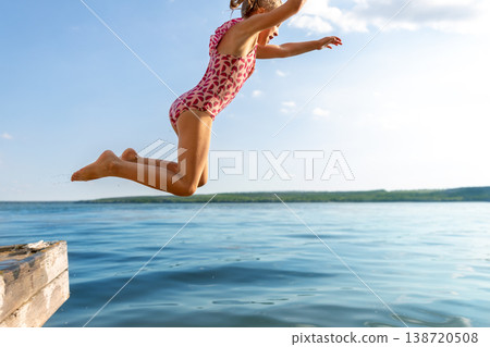 Little cute kid girl in swimsuit have fun enjoy pretend flying jumping from pier dock in clean blue water sea river or ocean on hot summer evening sunset. Carefree children lifestyle vacation concept Little cute kid girl in swimsuit have fun enjoy pretend flying jumping from pier dock in clean blue water sea river or ocean on hot summer evening sunset. Carefree children lifestyle vacation concept 138720508