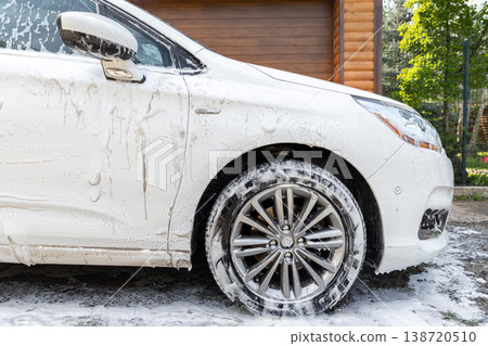 Close-up detail car wash with high pressure water equipment pump at home backyard outdoor on bright shiny summer day. Vehicle covered with foam shampoo chemical detergents during carwash self service Close-up detail car wash with high pressure water equipment pump at home backyard outdoor on bright shiny summer day. Vehicle covered with foam shampoo chemical detergents during carwash self service 138720510