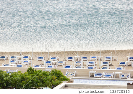 Rows loungers stand unused quiet seaside resort beach beside calm water pale sand, symbolizing tourism crisis weak season. Empty coastline still sea reflect decline of travel demand Rows loungers stand unused quiet seaside resort beach beside calm water pale sand, symbolizing tourism crisis weak season. Empty coastline still sea reflect decline of travel demand 138720515