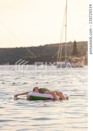 Woman float inflatable raft calm sea warm sunset light mediterranean harbor sailboat coastal landscape. Peaceful summer travel moment solitude relaxation wellness freedom vacation lifestyle outdoors Woman float inflatable raft calm sea warm sunset light mediterranean harbor sailboat coastal landscape. Peaceful summer travel moment solitude relaxation wellness freedom vacation lifestyle outdoors 138720534
