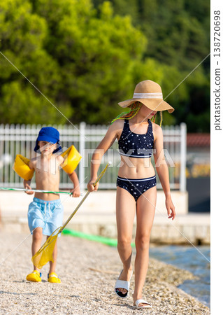 Children walking sunny beach holding fishing nets while exploring shoreline during summer vacation calm sea. Carefree seaside adventure playful childhood travel lifestyle family tourism atmosphere Children walking sunny beach holding fishing nets while exploring shoreline during summer vacation calm sea. Carefree seaside adventure playful childhood travel lifestyle family tourism atmosphere 138720698