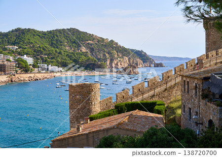 A picturesque view of Tossa de Mar, featuring the ancient castle walls overlooking a tranquil bay filled with boats on a clear day. A picturesque view of Tossa de Mar, featuring the ancient castle walls overlooking a tranquil bay filled with boats on a clear day. 138720700
