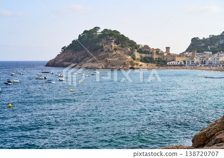 A picturesque view of Tossa de Mar, showcasing the historic castle perched on a rocky promontory overlooking the sea, with boats. 138720707