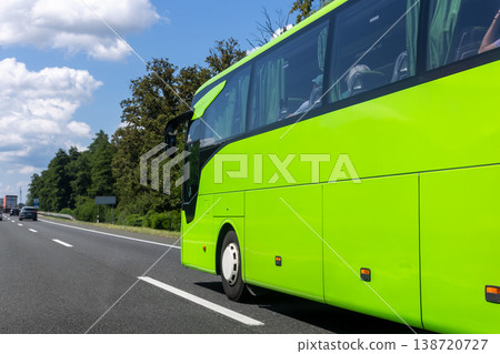 Bright green coach bus driving along highway through countryside under blue sky clouds. Passenger transport vehicle traveling on asphalt road during sunny summer day, concept tourism mobility journey Bright green coach bus driving along highway through countryside under blue sky clouds. Passenger transport vehicle traveling on asphalt road during sunny summer day, concept tourism mobility journey 138720727