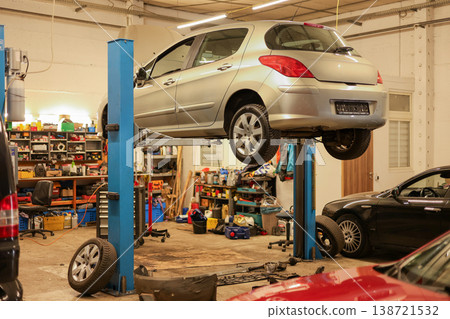 Passenger car elevated on hydraulic lift inside a professional auto workshop.  138721532