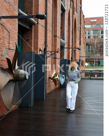 Woman Walking Along Industrial Brick Building With Marine Propellers And Urban Waterfront Woman Walking Along Industrial Brick Building With Marine Propellers And Urban Waterfront 138721713