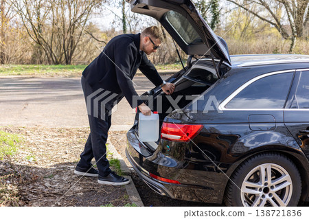 Man taking container from car trunk roadside situation fuel or emergency transport concept Man taking container from car trunk roadside situation fuel or emergency transport concept 138721836