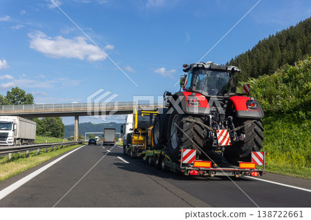 POV heavy industrial truck semi trailer flatbed platform transport big modern farming tractor machine on common alpine highway road bright day sky. Agricultural equipment transportation service work 138722661