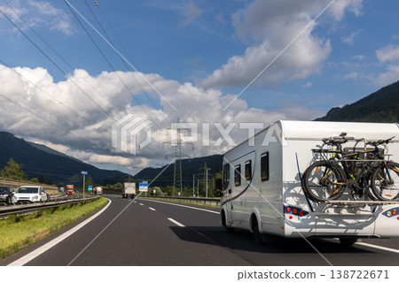 Scenic view big modern white family rv camper van vehicle drive Europe highway road alpine mountain blue sky summer day. Rving motorhome lifestyle travel and adventure tourism trip journey concept Scenic view big modern white family rv camper van vehicle drive Europe highway road alpine mountain blue sky summer day. Rving motorhome lifestyle travel and adventure tourism trip journey concept 138722671