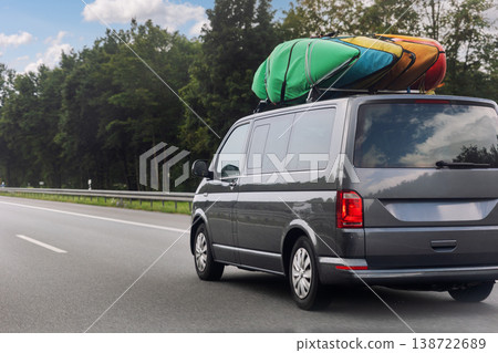Back view modern family van car with mounted roof rack many colorful kayak carrier driving european highway road against blue sky summer day. Lifestyle travel adventure trip journey concept Back view modern family van car with mounted roof rack many colorful kayak carrier driving european highway road against blue sky summer day. Lifestyle travel adventure trip journey concept 138722689