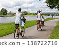 Family cycling along riverside bike path near Elbe in Magdeburg under dramatic clouds. Mother child riding bicycles helmets through green landscape symbol healthy lifestyle freedom summer recreation 138722716