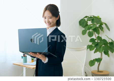 A young female business person in a suit is seen smiling and looking at the screen of her laptop, depicting an office work scene. A young female business person in a suit is seen smiling and looking at the screen of her laptop, depicting an office work scene. 138723500