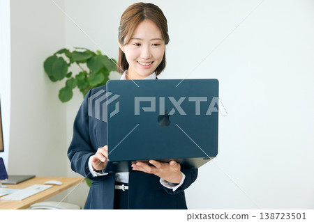 A young female business person smiles as she looks at the screen of her laptop in the office. 138723501