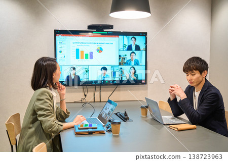 A man and woman from an IT company conduct an online meeting on a large monitor in the conference room. 138723963