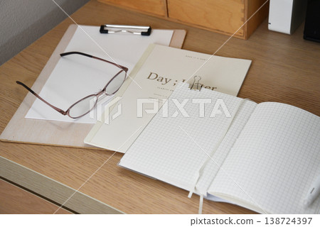 桌上放著筆記本、眼鏡和寫字板。 桌上放著筆記本、眼鏡和寫字板。 138724397
