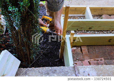 Man works with tools to build wooden steps frame around plants 138724501