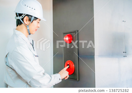A man in work clothes inspecting an automatic fire alarm system. 138725282