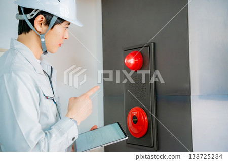 A man in work clothes inspecting an automatic fire alarm system. A man in work clothes inspecting an automatic fire alarm system. 138725284