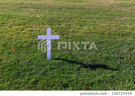 Grave cross surrounded by green lawn in a cemetery 138725438