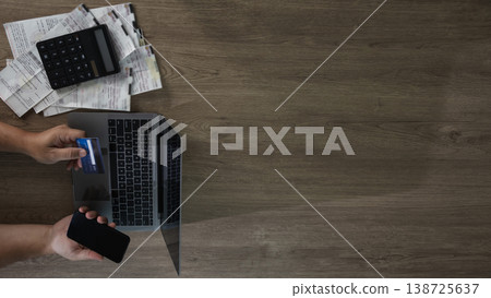 Top view of hands holding a smartphone and credit card over a laptop with receipts and a calculator on a desk, showing online payment, expense tracking, and personal finance. 138725637