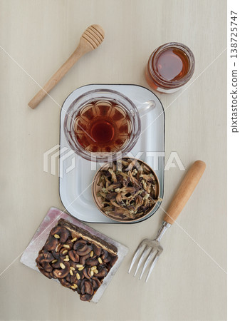 Enjoy a relaxing tea break with a rich toffee cheesecake garnished with cashews and chocolate almonds. It is served alongside butterfly pea flower tea and a jar of honey with a traditional wooden Enjoy a relaxing tea break with a rich toffee cheesecake garnished with cashews and chocolate almonds. It is served alongside butterfly pea flower tea and a jar of honey with a traditional wooden 138725747