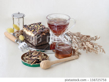 Herbal tea paired with sweet treats - a Toffee Cheesecake topped with cashews and chocolate-coated almonds, served with Butterfly Pea tea and honey in a small glass jar with a traditional wooden Herbal tea paired with sweet treats - a Toffee Cheesecake topped with cashews and chocolate-coated almonds, served with Butterfly Pea tea and honey in a small glass jar with a traditional wooden 138725758