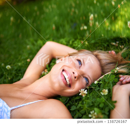 Spring, smile and relax with woman on grass in nature for calm, happy and peace. Park, flowers and field with face of female person lying in countryside meadow for summer, vacation and wellness 138726167
