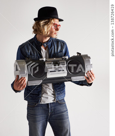 Boombox, fashion and retro style of a man in studio with music, radio or audio sound and noise. Male model person on a white background with denim outfit, glasses and hipster hat to listen to song Boombox, fashion and retro style of a man in studio with music, radio or audio sound and noise. Male model person on a white background with denim outfit, glasses and hipster hat to listen to song 138726419