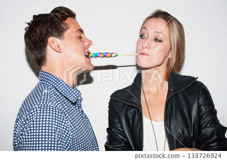 Lollipop, share and couple on a white background for love, bonding and playful with snacks. Dating, happy relationship and isolated of man and woman with sweets, sugar treats and candy in studio Lollipop, share and couple on a white background for love, bonding and playful with snacks. Dating, happy relationship and isolated of man and woman with sweets, sugar treats and candy in studio 138726924