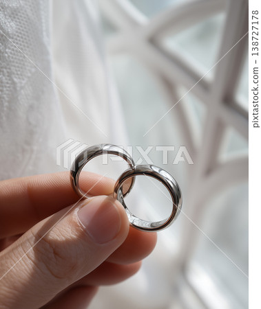 Elegant Close Up of Slender Fingers Holding Silver Mobius Couple Rings by Window Light 138727178