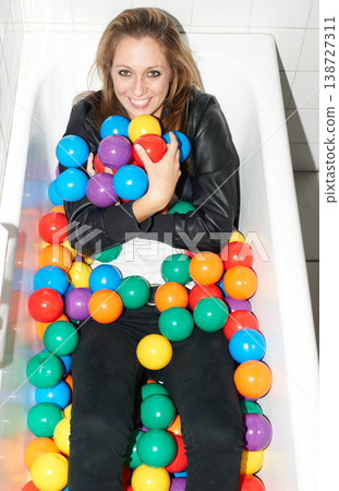 Portrait, balls and happy woman in bathtub for fashion, style and trendy hipster at home. Smile of person in tub with color, sphere and plastic with body in bathroom, relax in edgy and cool clothes Portrait, balls and happy woman in bathtub for fashion, style and trendy hipster at home. Smile of person in tub with color, sphere and plastic with body in bathroom, relax in edgy and cool clothes 138727311