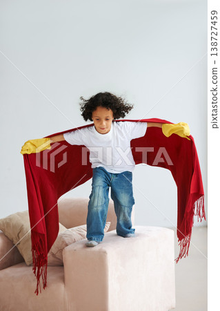 Jump, children and a boy superhero in a costume on a sofa in the living room of his home for playing a game. Flying, growth and fantasy with a young kid in a cape for justice or safety cosplay Jump, children and a boy superhero in a costume on a sofa in the living room of his home for playing a game. Flying, growth and fantasy with a young kid in a cape for justice or safety cosplay 138727459