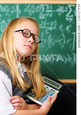 Child, portrait and calculator by chalkboard for education, learning and problem solving or solution with confidence. Smart kid, student or girl with glasses for school, numbers and math in classroom 138727534