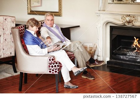 Senior couple, relax and reading by fire place on holiday, retirement or vacation together at hotel or resort. Man and woman sitting with magazine or paper for news, deals or activities at house Senior couple, relax and reading by fire place on holiday, retirement or vacation together at hotel or resort. Man and woman sitting with magazine or paper for news, deals or activities at house 138727567
