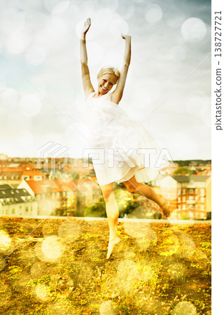 Portrait, freedom and jump with a woman on a roof in the city and fun against a bokeh effect. Smile, neighborhood or arms raised and a happy young person with energy outdoor to dance in summer 138727721