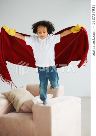 Fly, children and a boy superhero in a costume on a sofa in the living room of his home for playing a game. Jumping, growth and fantasy with a young kid in a cape for justice or safety cosplay Fly, children and a boy superhero in a costume on a sofa in the living room of his home for playing a game. Jumping, growth and fantasy with a young kid in a cape for justice or safety cosplay 138727935