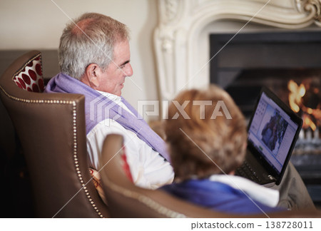 Relax, senior couple with laptop in hotel lounge or restaurant checking social media on retirement vacation. Computer, old man and woman at fireplace in cozy holiday accommodation with online search. 138728011