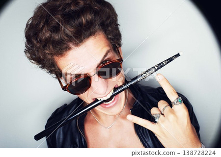 Rock man, horns and studio portrait with drumstick, sunglasses or biting in spotlight by white background. Punk musician, drummer or artist with emoji, icon and hand sign for performance at concert 138728224