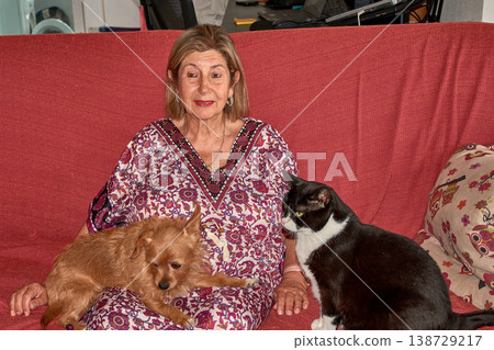 An elderly woman shares a sofa with her small ginger dog and her large black cat in a warm, homey atmosphere. An elderly woman shares a sofa with her small ginger dog and her large black cat in a warm, homey atmosphere. 138729217