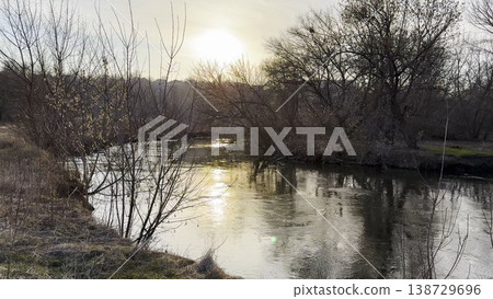 View on calm river in early spring reflects soft sunlight. Warm rays shimmer on water surface, creating peaceful at sunset. The image conveys tranquility and seasonal awakening in nature. Slow motion 138729696