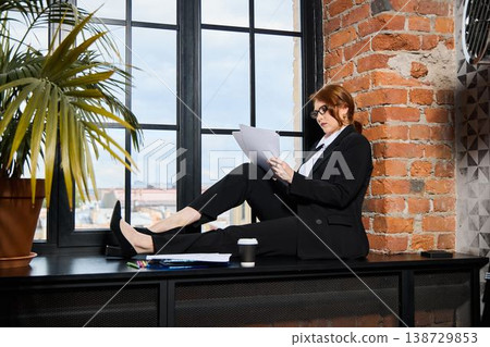 Focused woman in modern workspace with paperwork and beverage Focused woman in modern workspace with paperwork and beverage 138729853