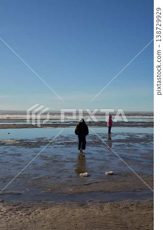 People Depart Shoreline. Persons Strolling Away Across Moist Shoreline With Shadows And Reflections 138729929