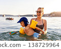Mother laughing have fun hold child sea swim warm summer sunset. Joyful family vacation candid moment expression playful kid wear armbands splashing water calm seaside coastline travel destination 138729964