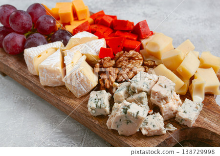 Assorted cheese on a wooden board, with grapes and walnuts, appetizer, no people. 138729998