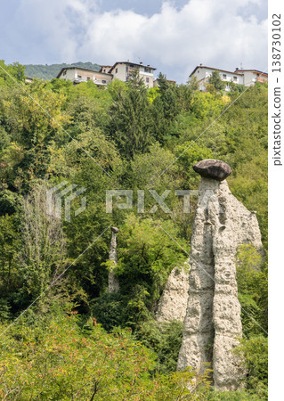 Zone Rock Pyramids in Lombardy with tall white hoodoo capped by dark boulder above green woodland Zone Rock Pyramids in Lombardy with tall white hoodoo capped by dark boulder above green woodland 138730102