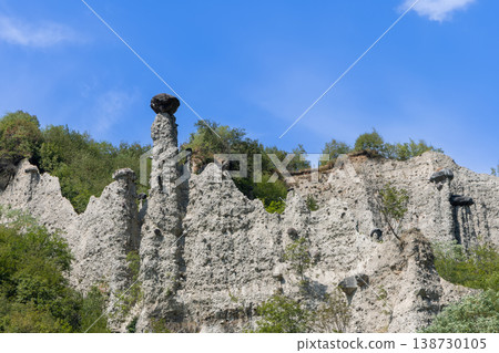 Jagged white cliffs of Pyramids of Zone with dark boulder crowning tallest earth column in Italy 138730105