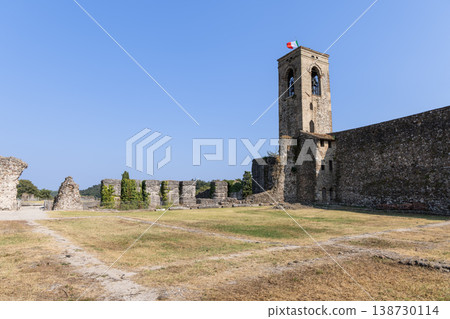 Cavriana castle bell tower and broad courtyard ruins in Lombardy under blue sky with Italian flag 138730114