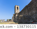 Medieval bell tower and castle wall in Cavriana with sunlit stone grass and vivid blue Lombardy sky 138730115