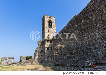 Medieval bell tower and castle wall in Cavriana with sunlit stone grass and vivid blue Lombardy sky Medieval bell tower and castle wall in Cavriana with sunlit stone grass and vivid blue Lombardy sky 138730115
